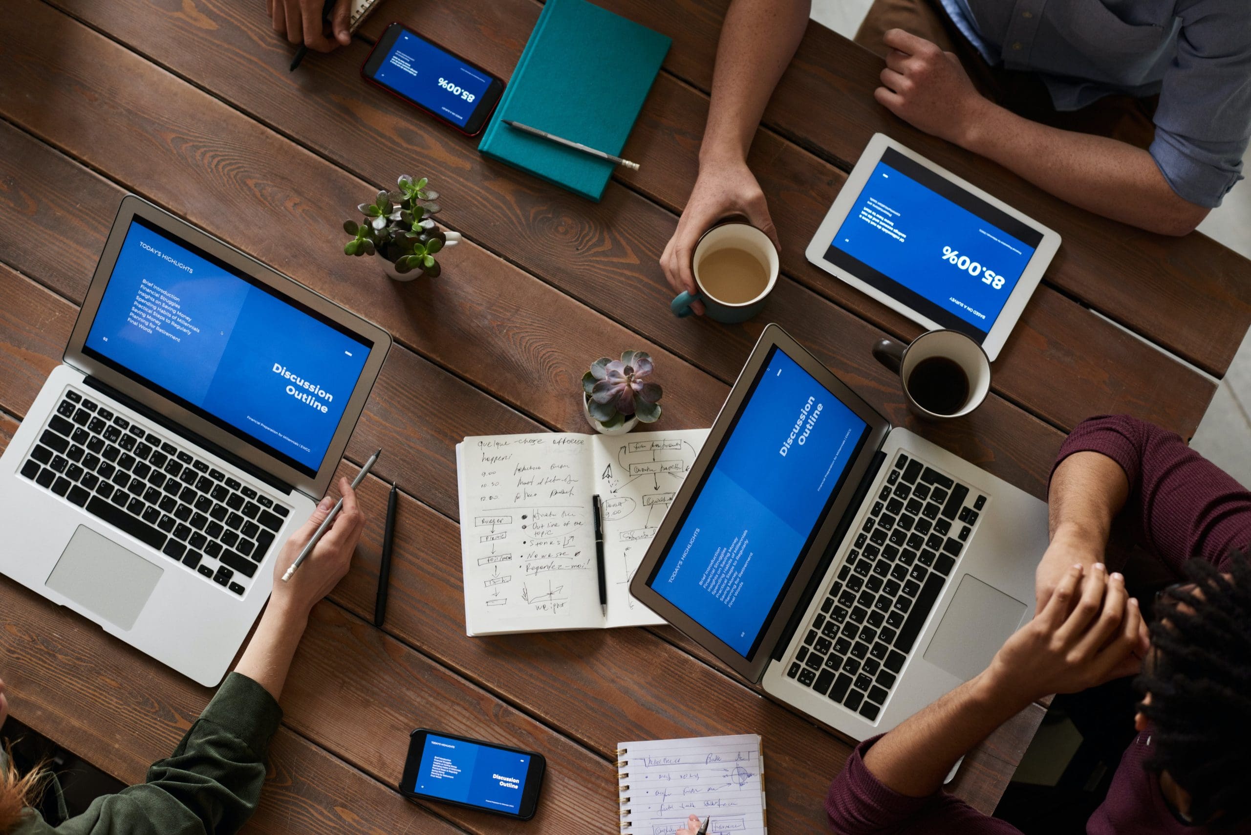 View on top of a table with tablets and desktop. You can also see some hands and coffee.